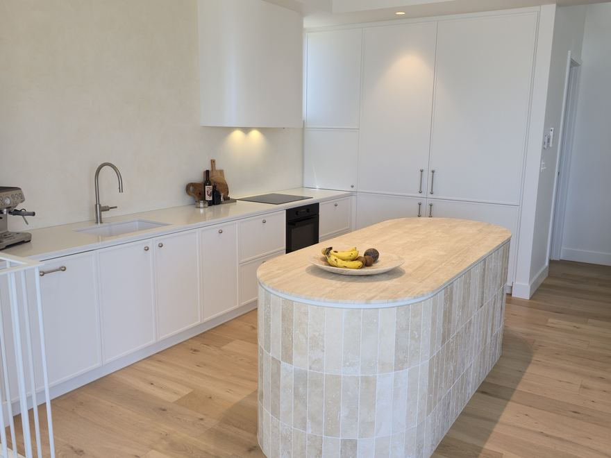 White custom kitchen with a wide stone island bench and integrated appliances