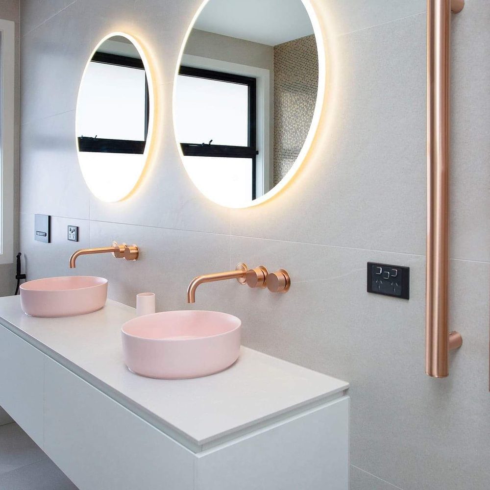 Double vanity with round backlit mirrors, brass tapware, and sculptural basins