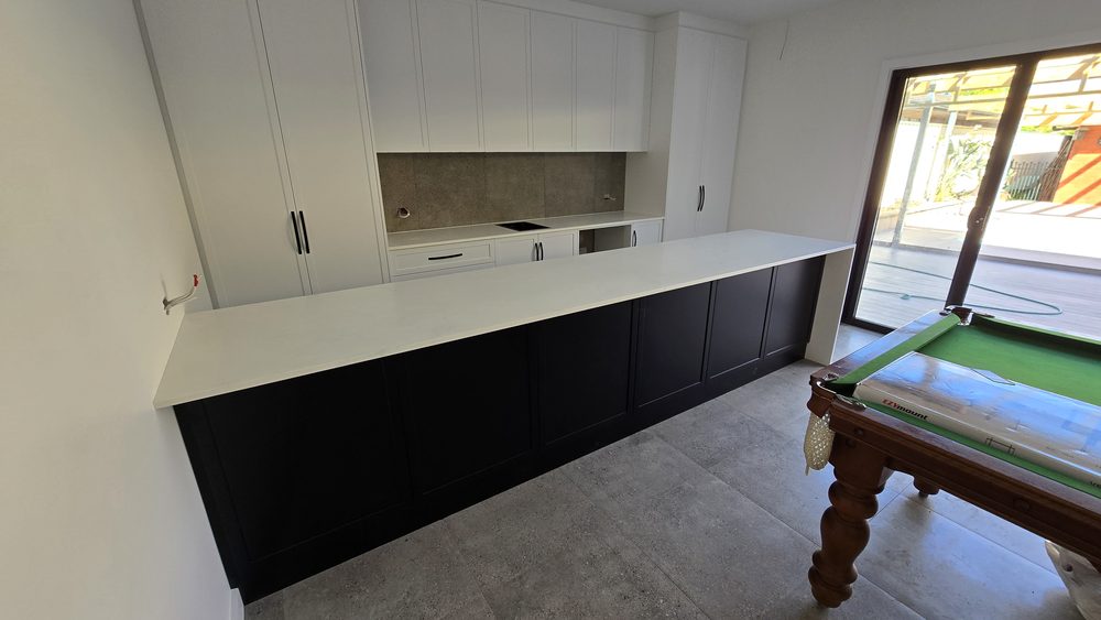 Custom kitchen with a long stone benchtop, dark cabinetry, and stone splashback