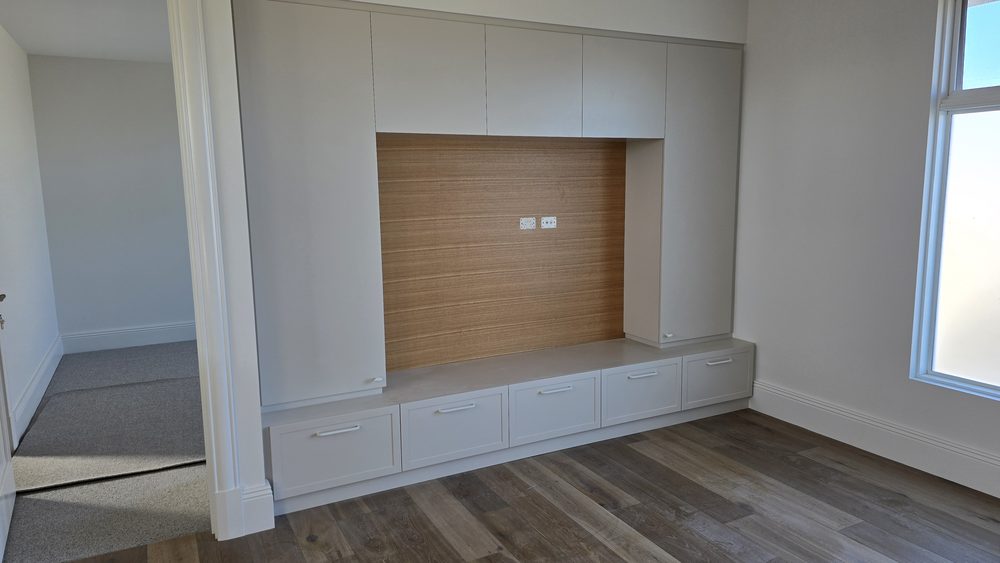 Custom built-in media wall with a timber-lined TV recess and white cabinetry