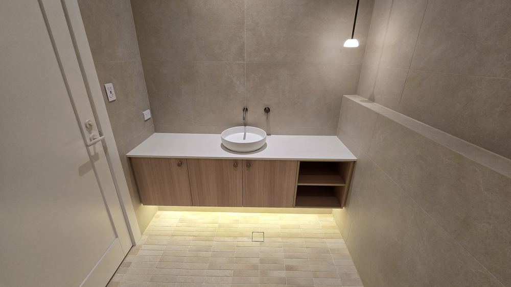Floating timber vanity with a stone benchtop, round vessel basin, and LED underlighting against large-format stone-look tiles