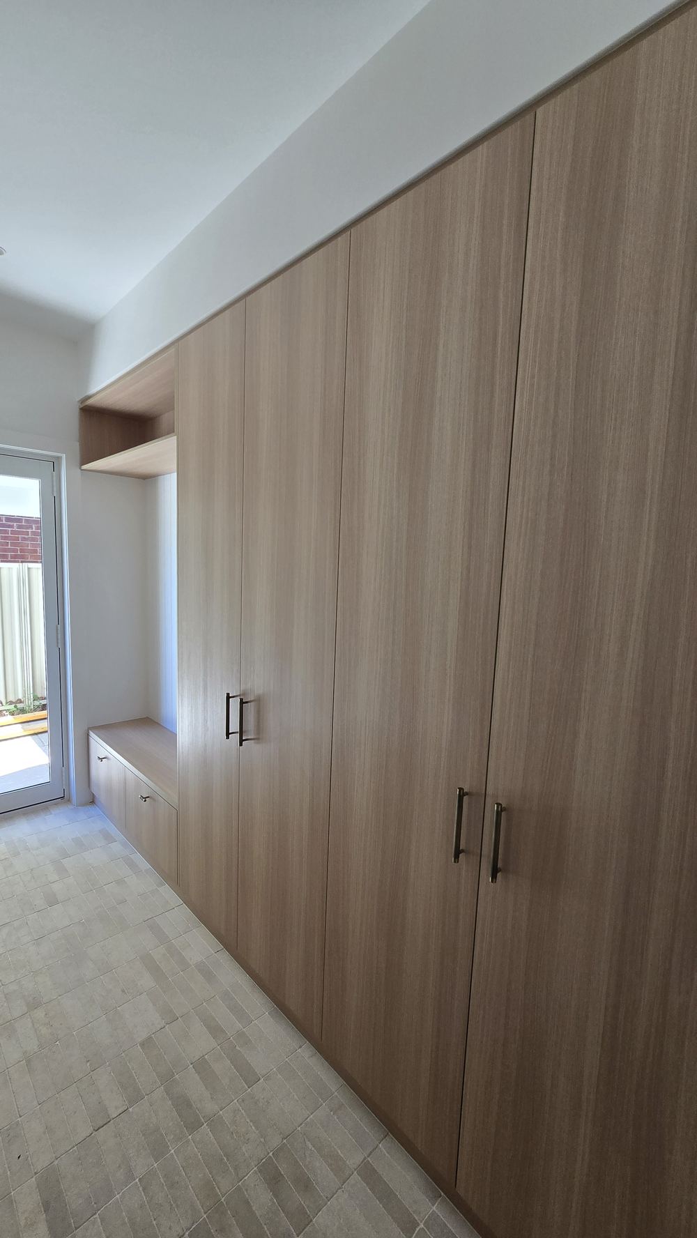 Floor-to-ceiling timber-look built-in wardrobe with a bench seat beside a glass door