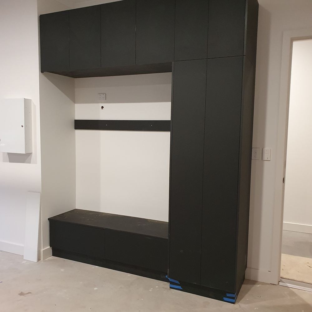 Dark built-in storage unit with overhead cabinets, a bench seat, and a full-height cupboard