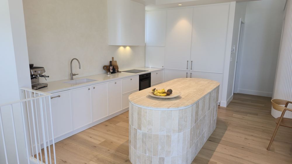 White custom kitchen with wide stone island bench and integrated appliances