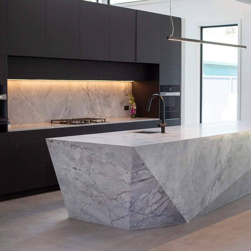 Marble waterfall island bench with under-bench lighting in a dark-toned kitchen