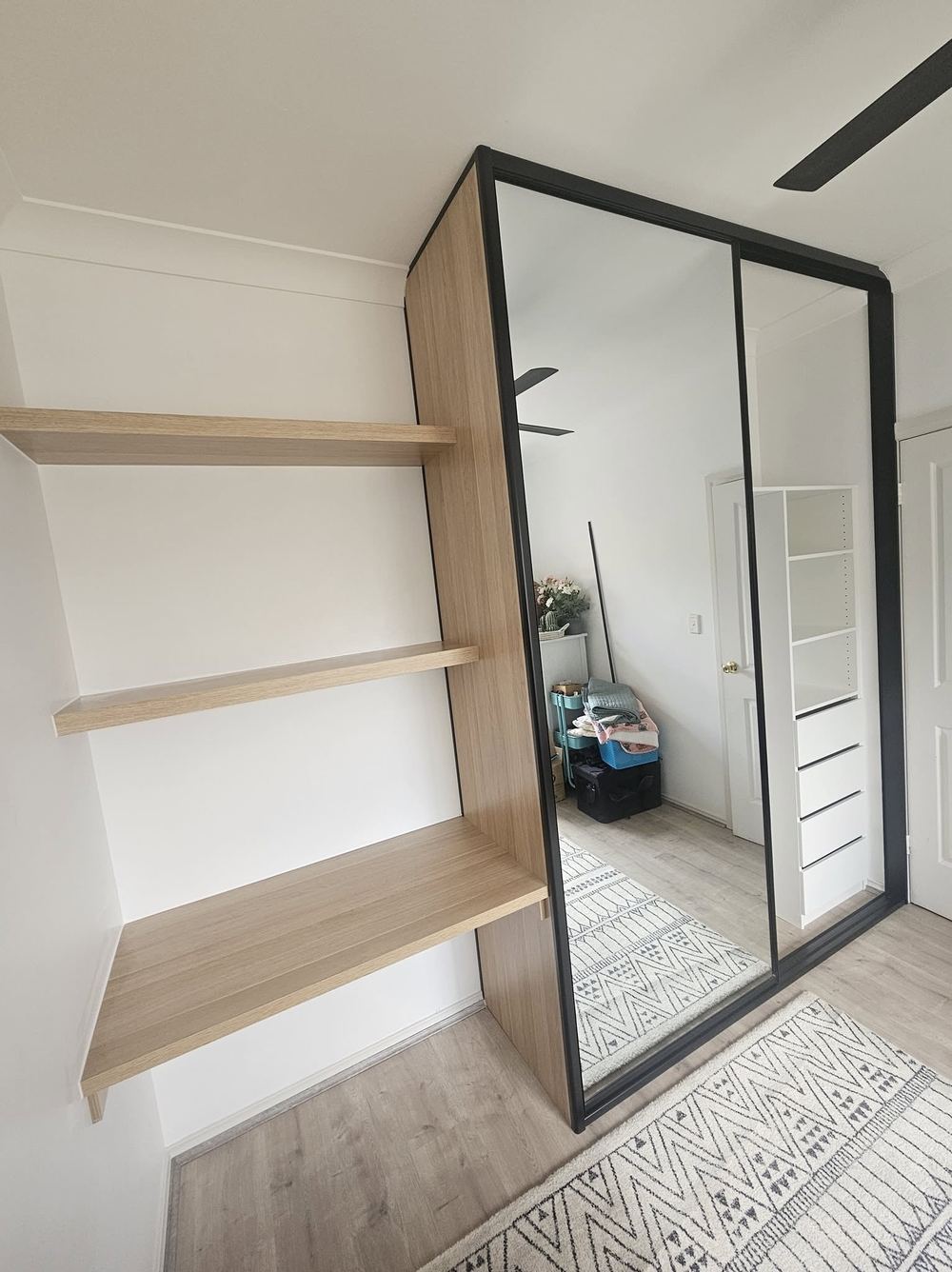 Walk-in wardrobe with a black-framed mirror robe and floating timber shelves