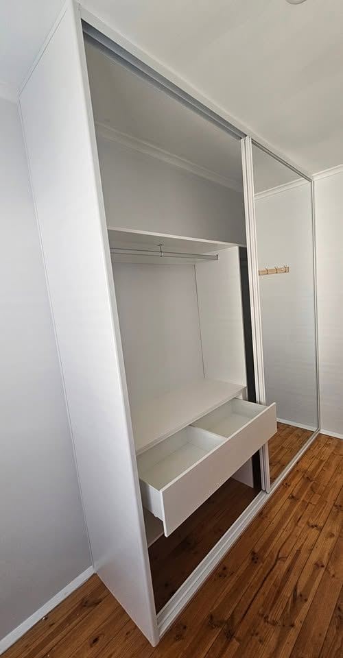 White built-in sliding wardrobe with mirror doors, internal shelving, and a hanging rail