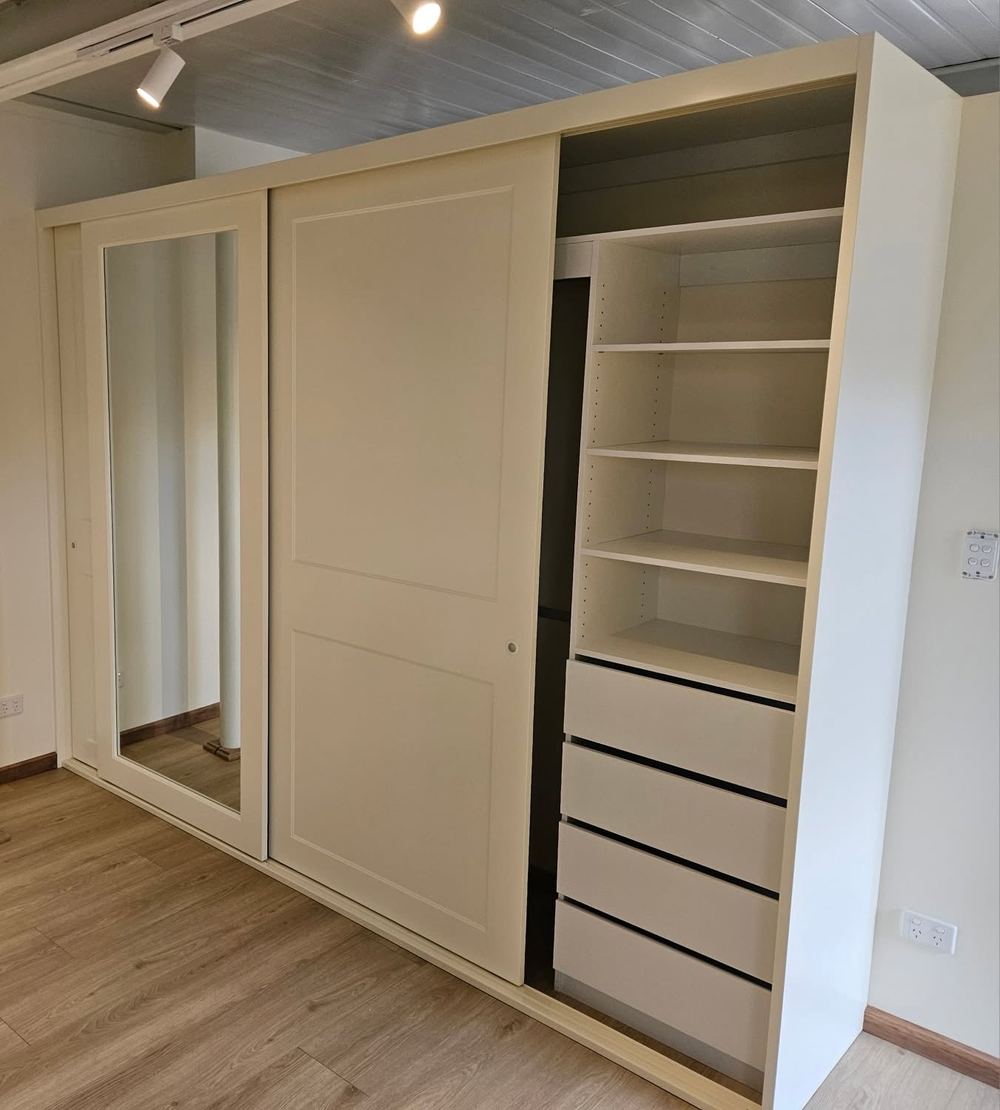 Cream sliding wardrobe with a mirror panel and fitted internal shelving and drawers