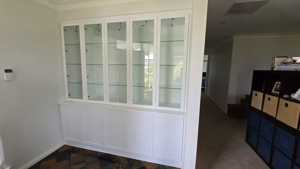 Custom built-in display cabinet with glazed doors beside a window seat