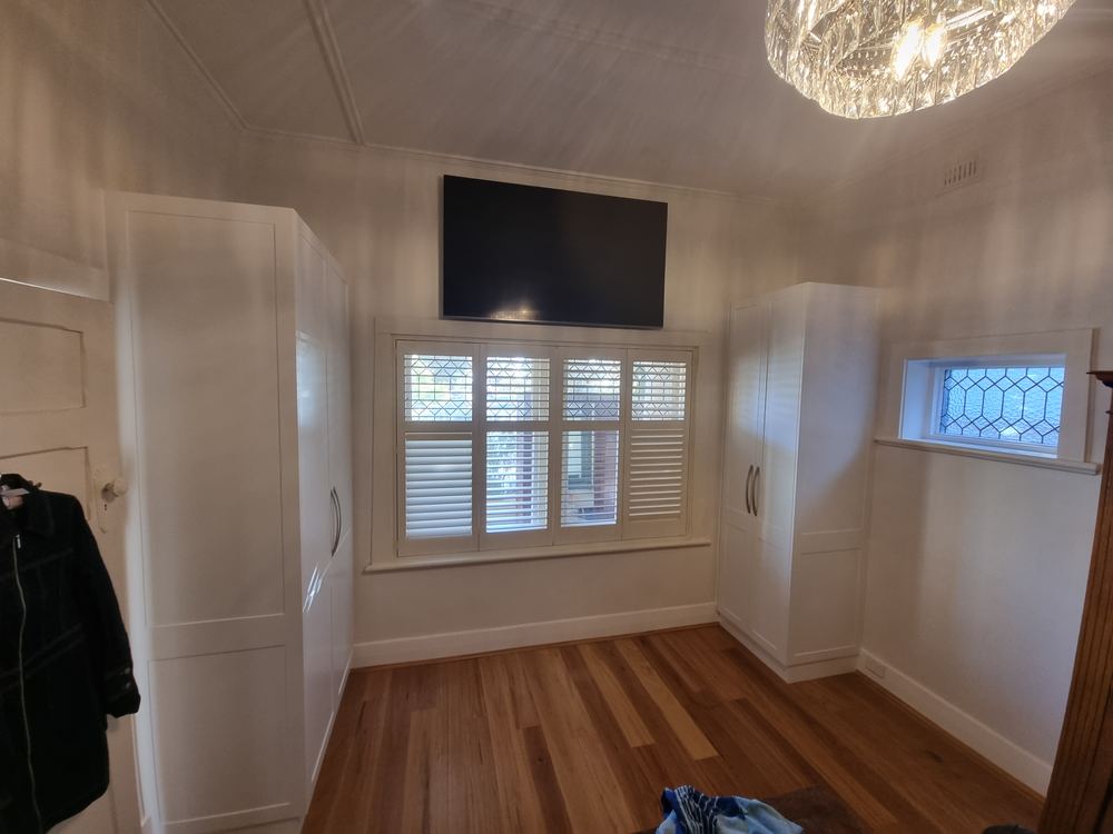White built-in wardrobes wrapping around bedroom windows