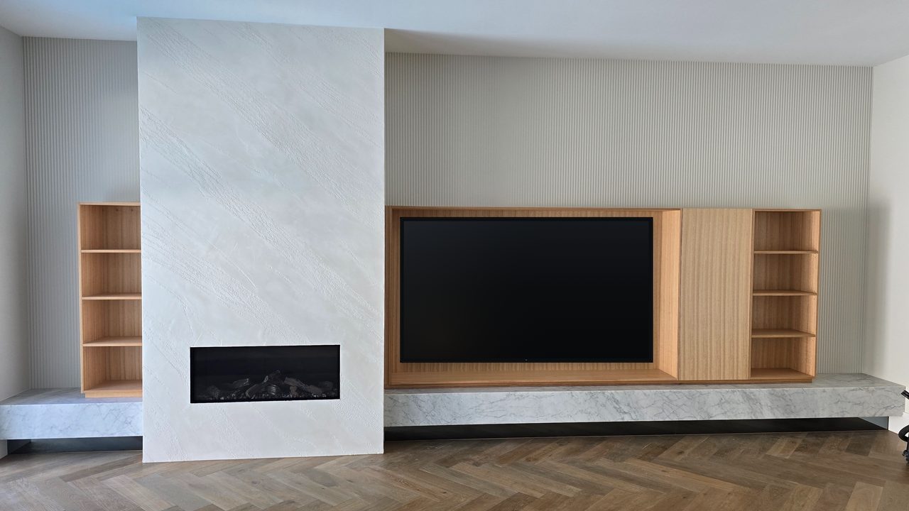 Custom timber media wall with a rendered fireplace, built-in shelving, and a marble hearth over herringbone timber floors