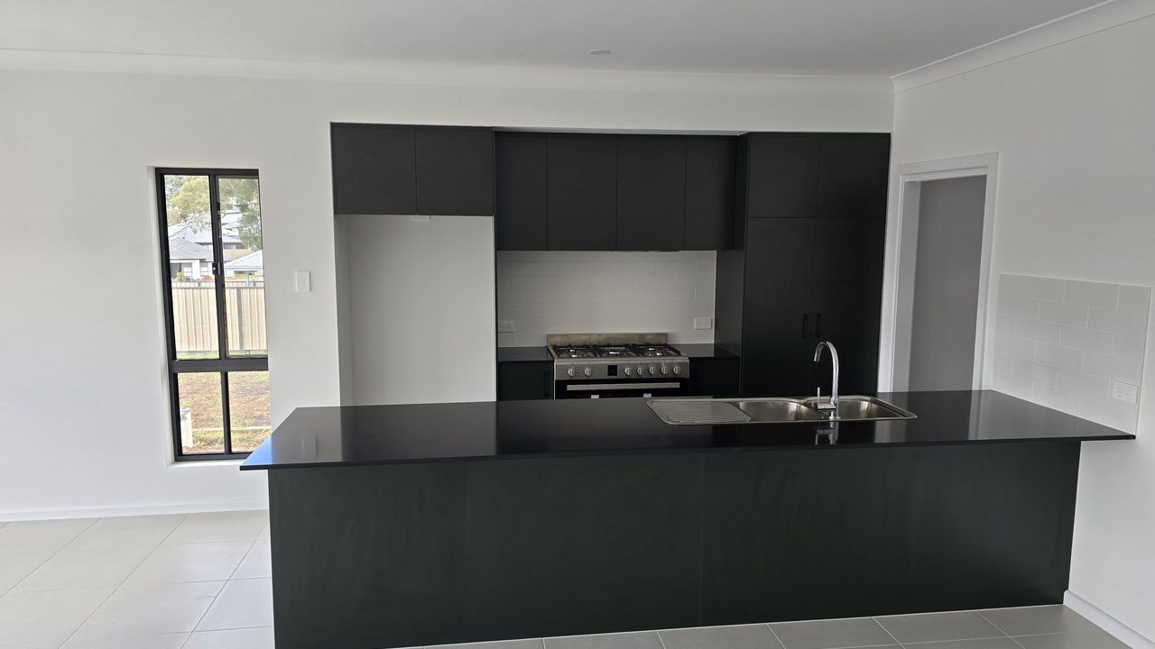 Open-plan kitchen with a large dark island bench, stainless steel sink, and dark cabinetry