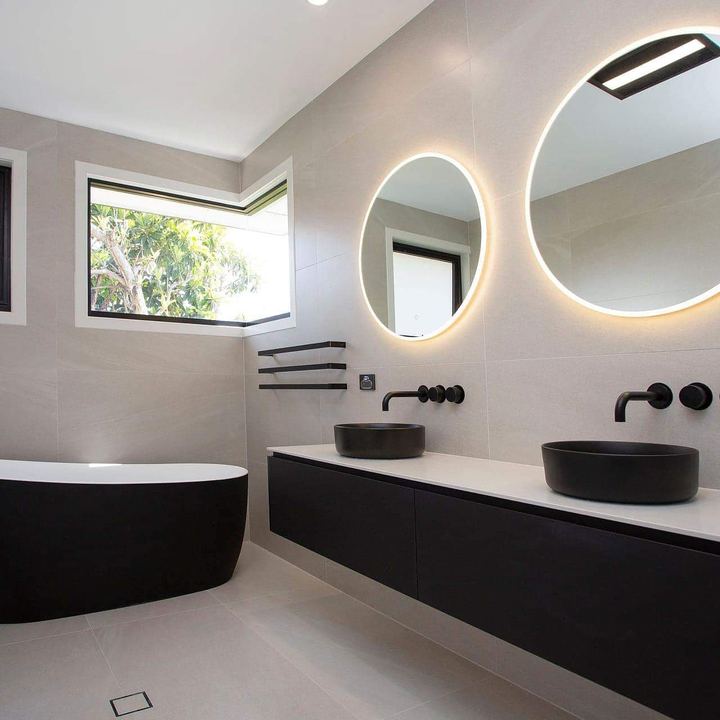 Double vanity with round backlit mirrors, brass tapware, and a sculptural pink basin